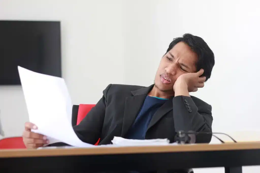 Ondernemer aan bureau omringd door papieren, voelt zich overweldigd en uitgeput door werkdruk