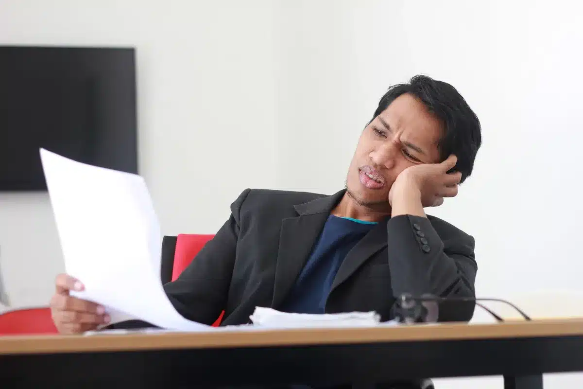 Ondernemer aan bureau omringd door papieren, voelt zich overweldigd en uitgeput door werkdruk