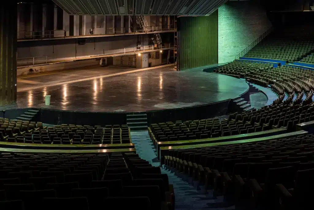 Theatercriticus zittend in een theaterzaal met notitieboekje, kijkend naar een verlicht podium