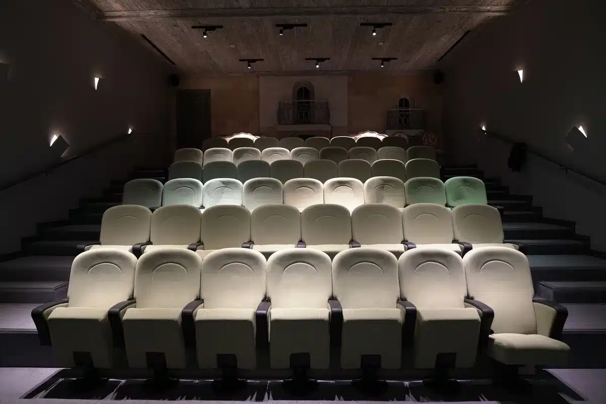 Nieuwe theaterstoelen met houten armleuningen in een gerenoveerde theaterzaal met LED-verlichting.