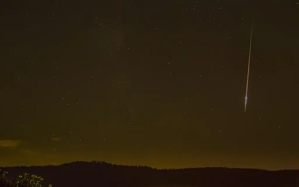 Nachtelijke hemel met vallende sterren en meteorensporen boven een donker landschap