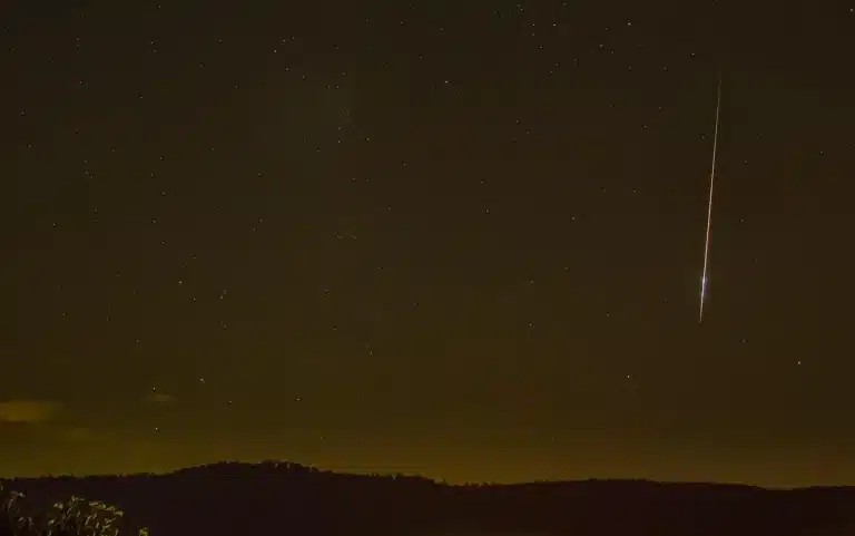 Nachtelijke hemel met vallende sterren en meteorensporen boven een donker landschap