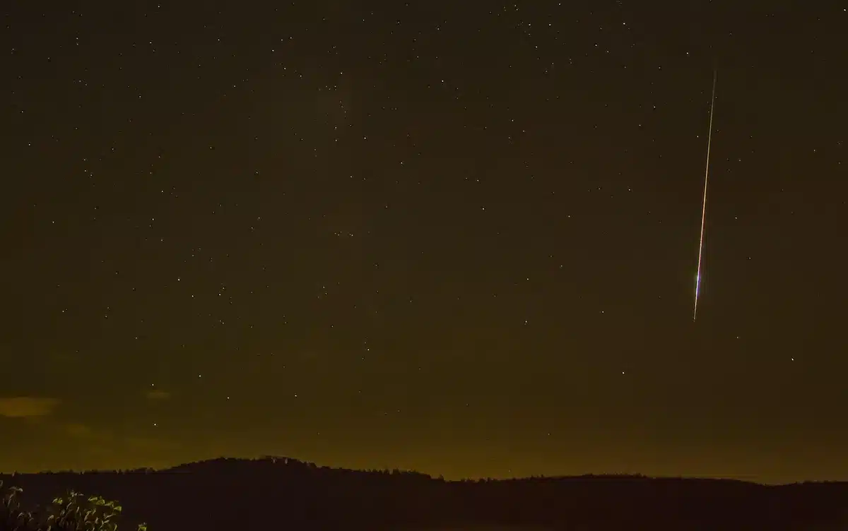 Nachtelijke hemel met vallende sterren en meteorensporen boven een donker landschap